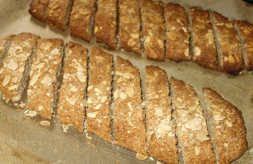 Skivade havrekakor med mandel på en bakplåt, med en gyllene yta och tydliga snitt.